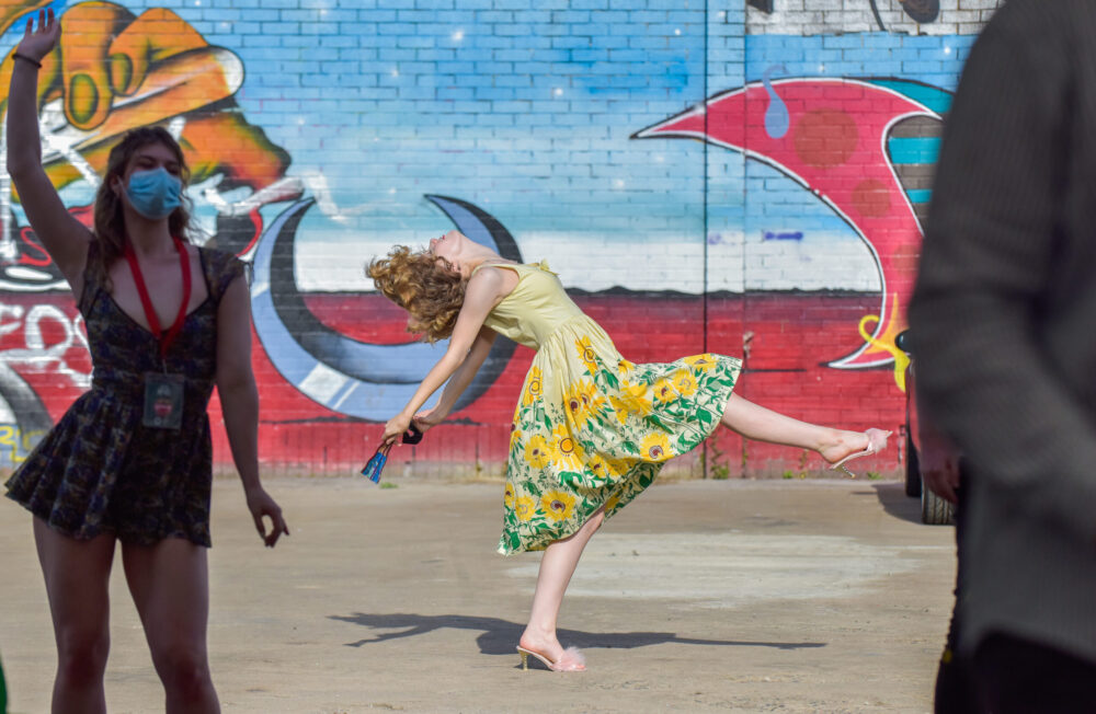 Scottish Opera Young Company rehearse for Kurt Weill's 'Tsar Has His Photograph Taken'. Woman in yellow dress performs a scene from an outdoor opera performance.
